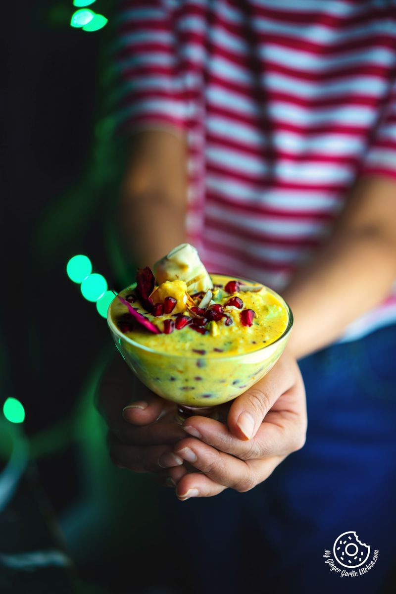 a person holding fruit rabri in a transparent dessert glass