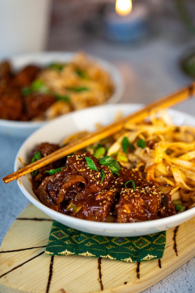 Crispy gochujang tofu with glossy spicy-sweet sauce, sesame seeds, spring onions, and noodles in a bowl