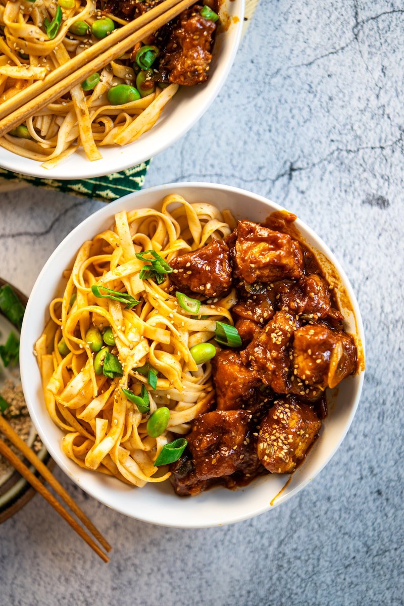 Close-up of crispy gochujang tofu coated in glossy spicy-sweet sauce with sesame seeds and spring onions