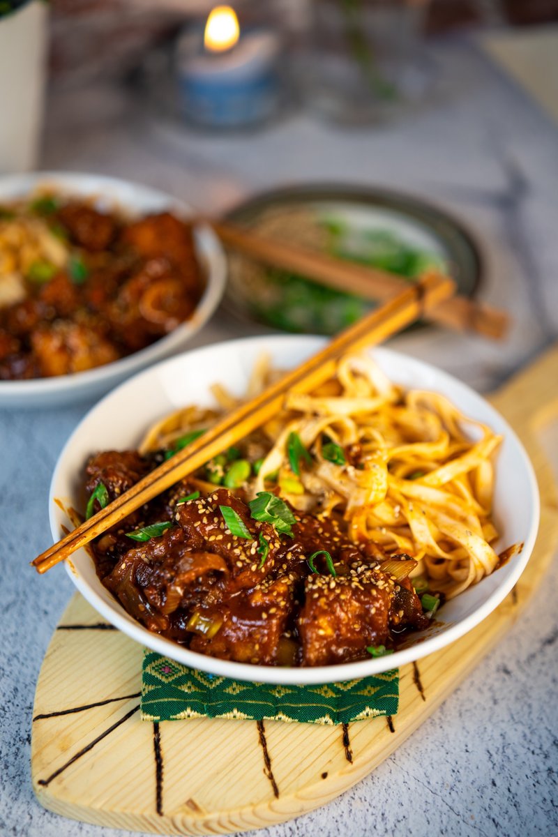 Crispy air fryer gochujang tofu served with udon noodles, edamame, sesame seeds, and spring onions