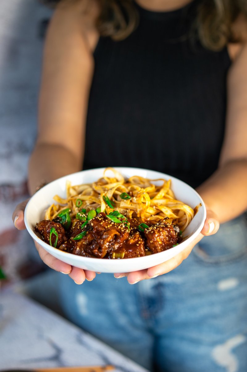Homemade crispy gochujang tofu with udon noodles, sesame seeds, and spring onions served in a bowl