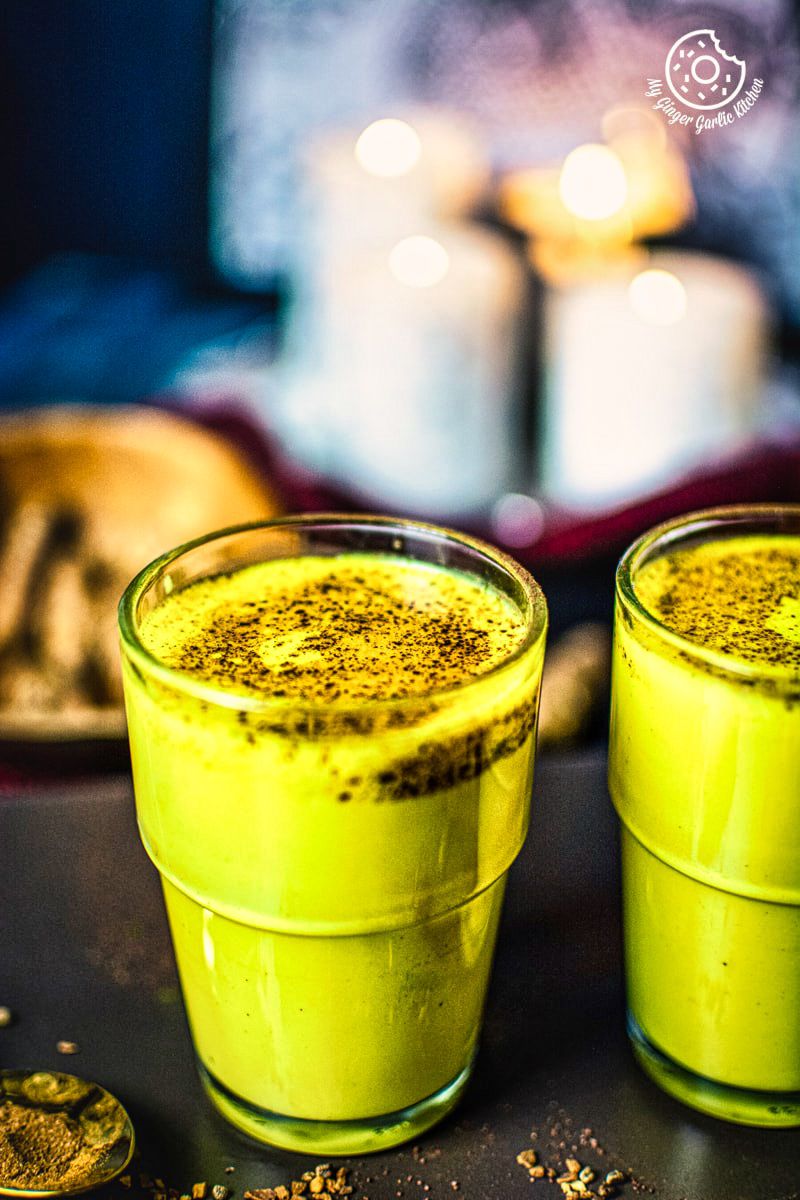 Golden milk (haldi doodh) glasses and some turmeric root and candles in background
