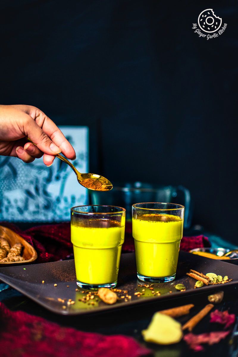 a hand with a golden spoon and golden milk (haldi doodh) glasses