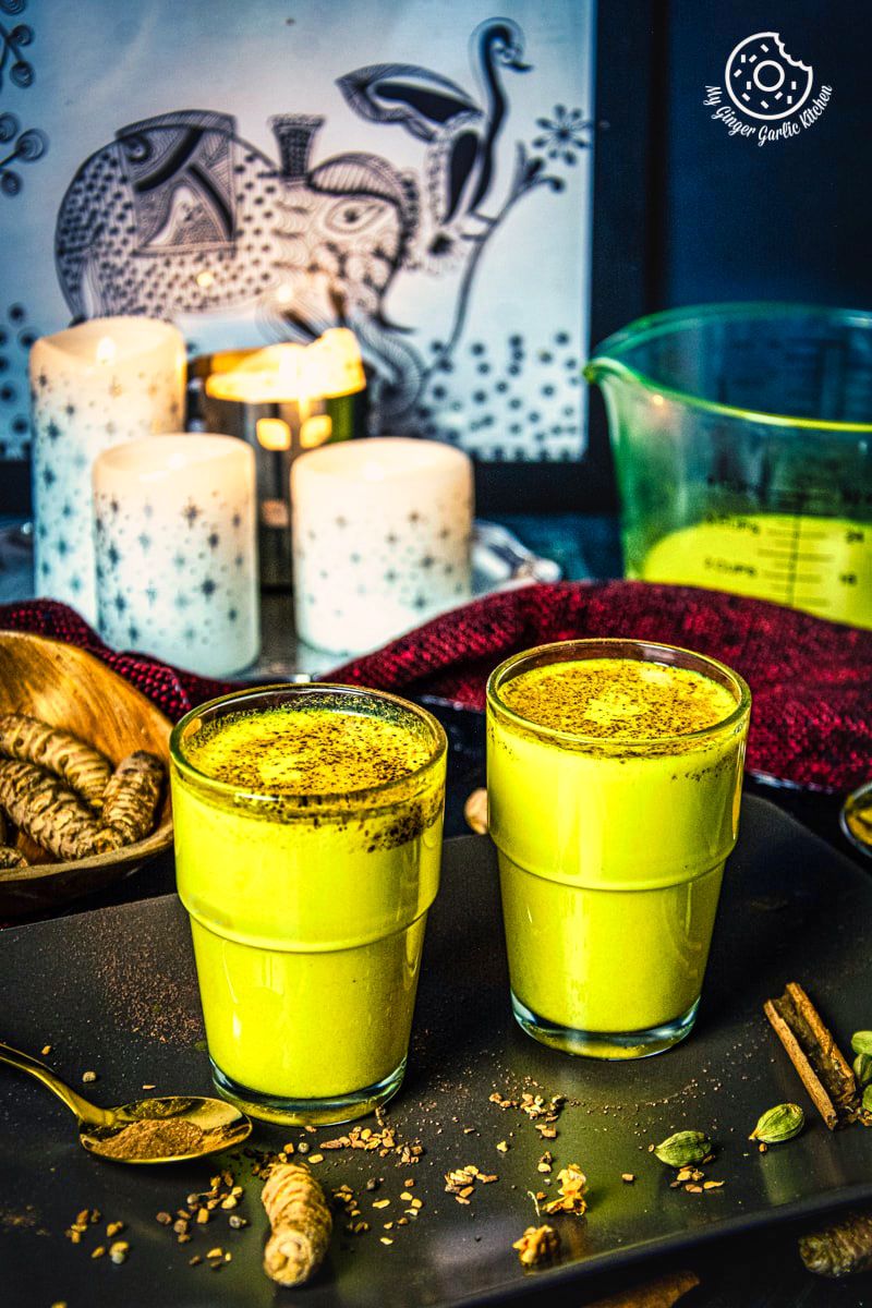 2 glasses of turmeric milk (haldi doodh) served in a brown tray with some spices