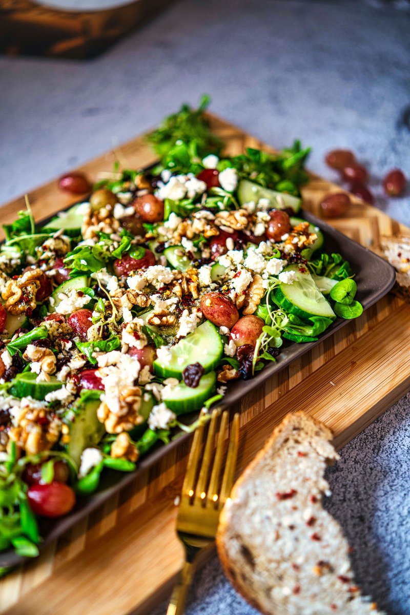 Close-up of a colorful grape salad sprinkled with crumbled feta and walnuts, ready to be served at a casual dining setting.