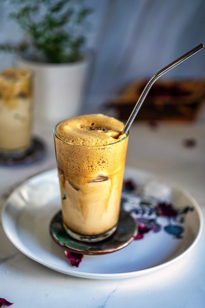 Greek frappe in a tall glass with a metal straw on a marble surface, surrounded by dried flowers.