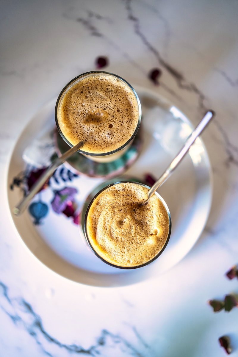 Top view of two glasses of Greek frappe with frothy tops on a marble table, garnished with dried petals.