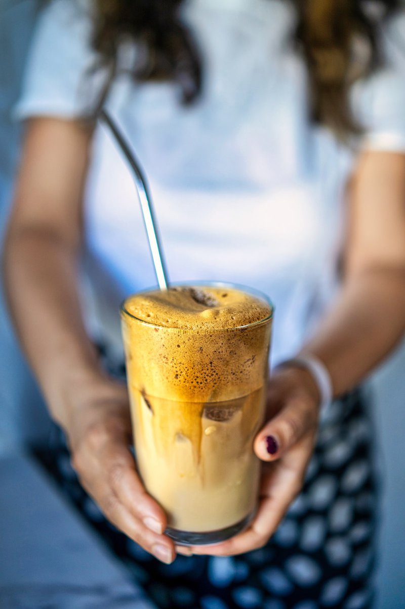 Woman holding a glass of Greek frappe with a metal straw, ready to drink.