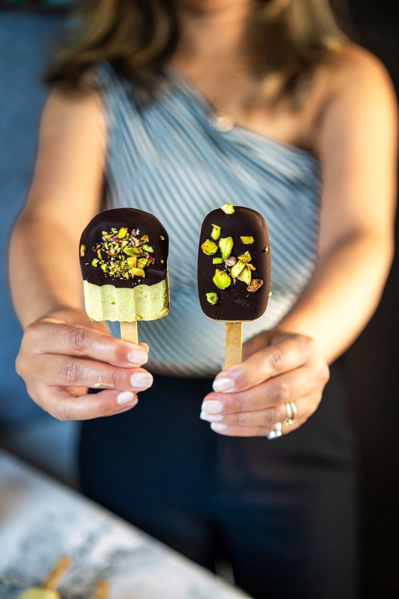 Greek yogurt pistachio ice cream bars dipped in dark chocolate and topped with roasted pistachios, held by hand