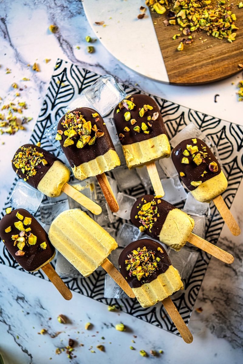 Homemade Greek yogurt pistachio ice cream bars with dark chocolate coating and roasted pistachios arranged over ice
