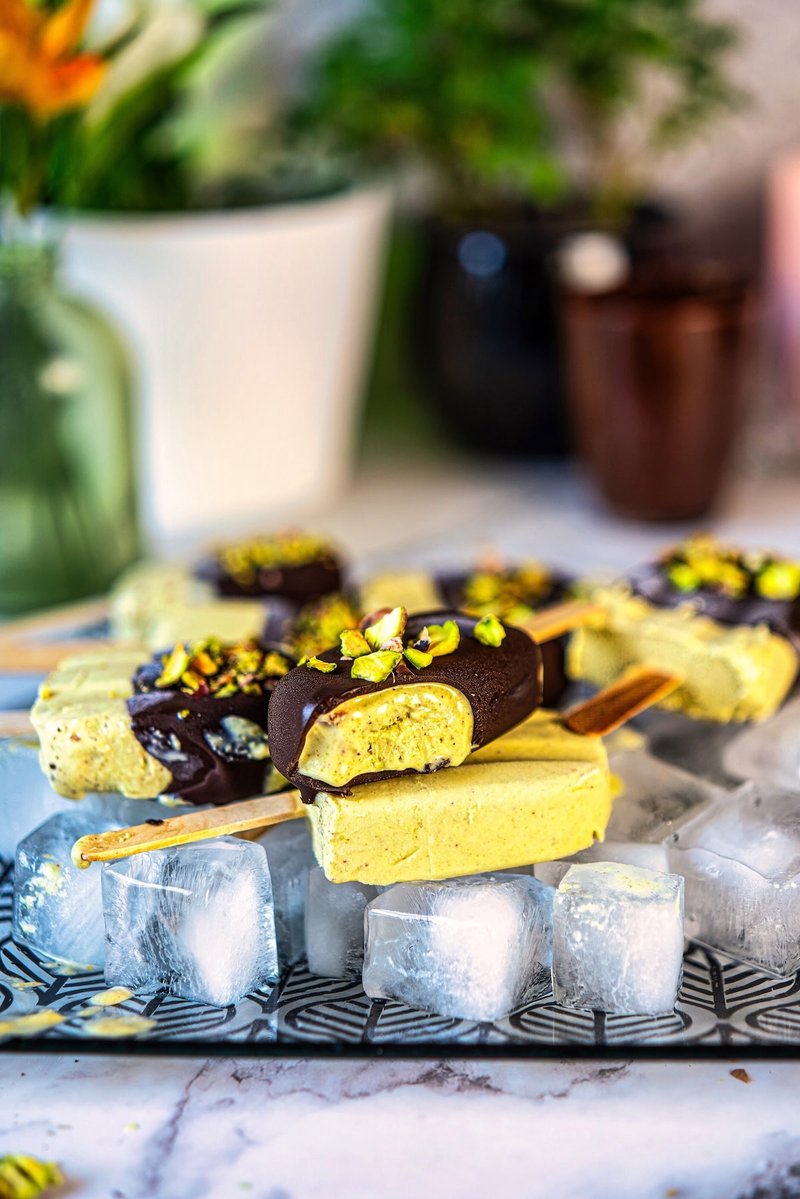 Homemade pistachio ice cream bars with Greek yogurt, dark chocolate coating, and chopped pistachios served over ice