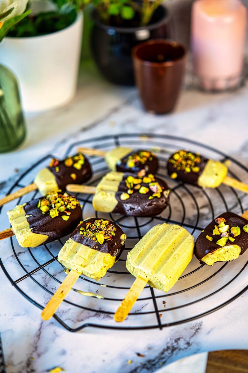 Greek yogurt pistachio ice cream bars with dark chocolate coating and pistachio topping arranged on a cooling rack