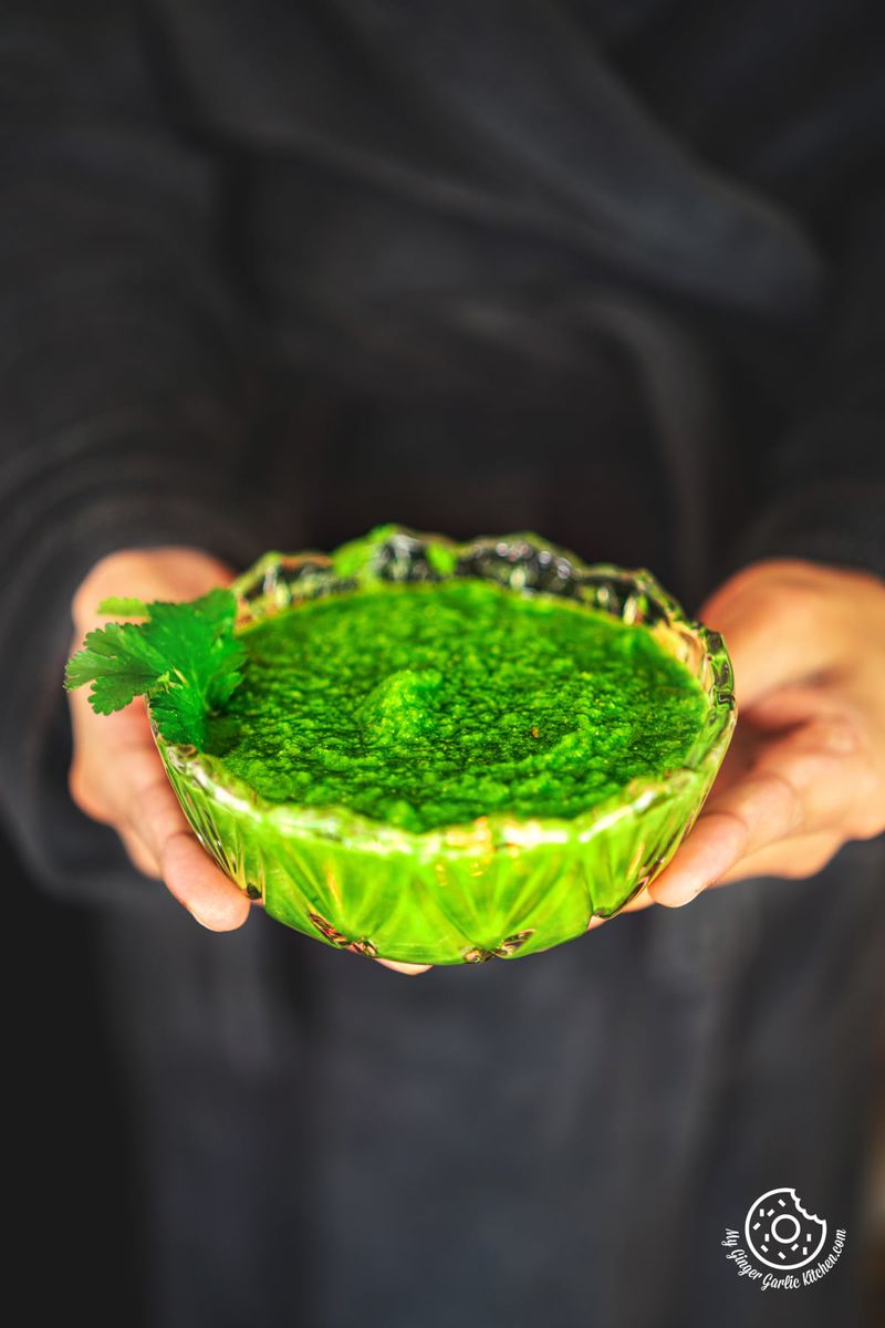 photo of a person holding a bowl of green mango chutney with a coriander leaf decoration