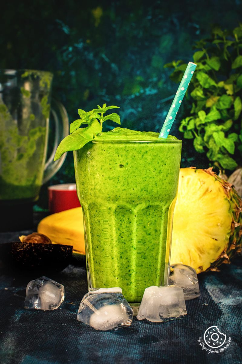 green smoothie in a tall glass and pineapple in background