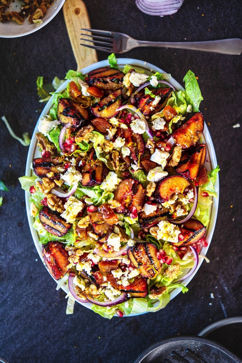 Overhead view of grilled plum salad with caramelized plums, feta, walnuts, dried apricots, and pomegranate