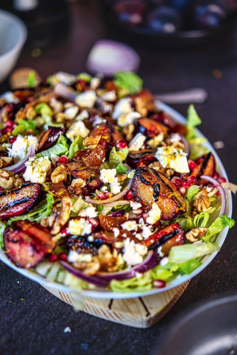 Close-up of grilled plum salad with caramelized plums, feta cheese, walnuts, red onion, and pomegranate