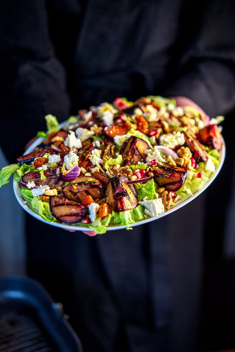 Grilled plum salad held on a platter with caramelized plums, feta, walnuts, and pomegranate