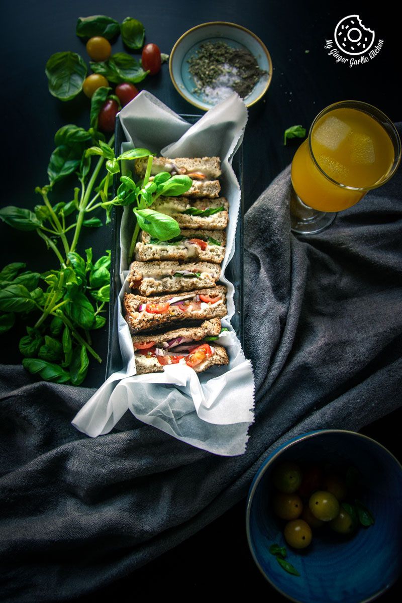 a tray of grilled tomato mozzarella sandwiches and a glass of juice with tomatoes on a table