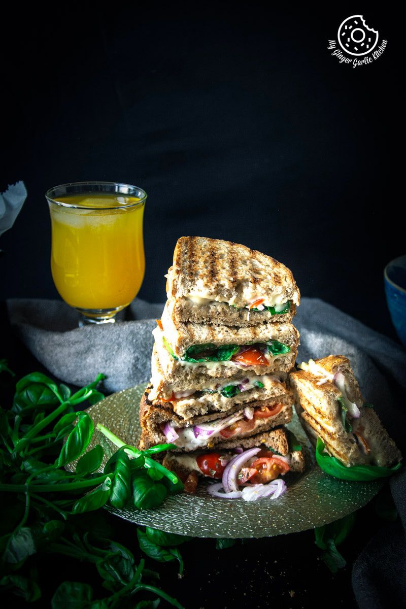 grilled tomato mozzarella sandwiches stacked on a plate with a glass of orange juice