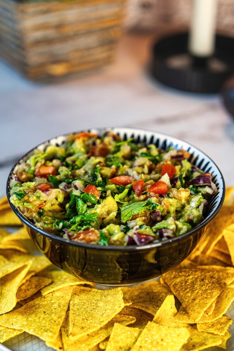 Close-up of a bowl of homemade guacamole garnished with diced tomatoes and onions, served with tortilla chips.