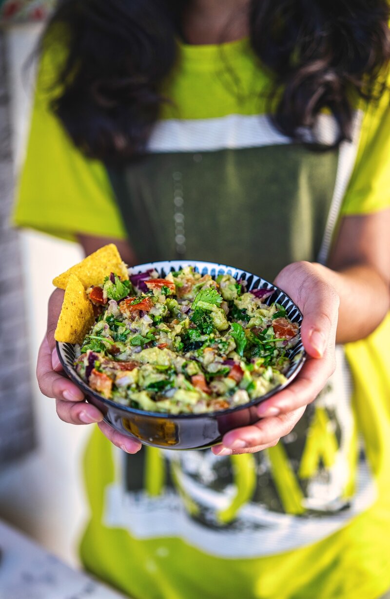 Person in a green shirt holding a bowl of guacamole with tortilla chips, ready to serve.