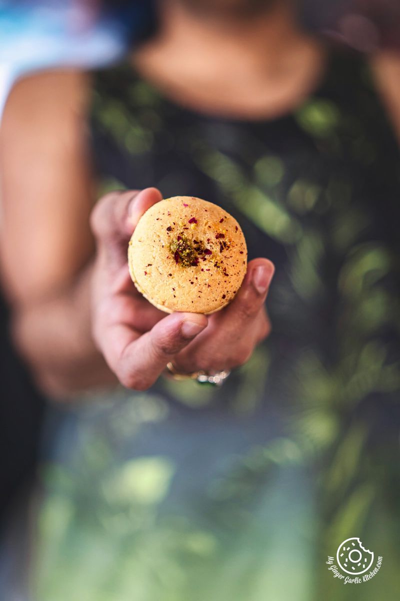 a man holding rose and pistachio decorated gulab jamun cookie