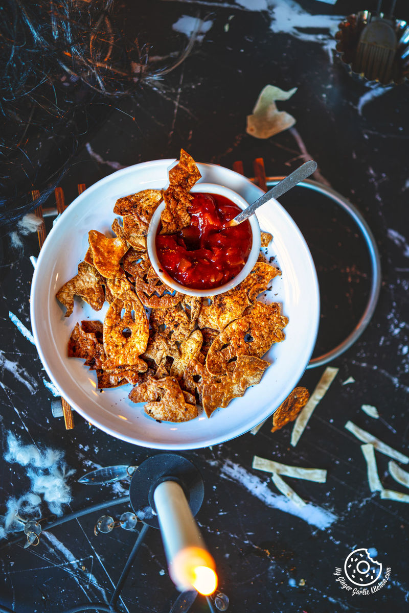 there is a plate of halloween tortilla chips that has a chip in it with a bowl of tomato salsa on it