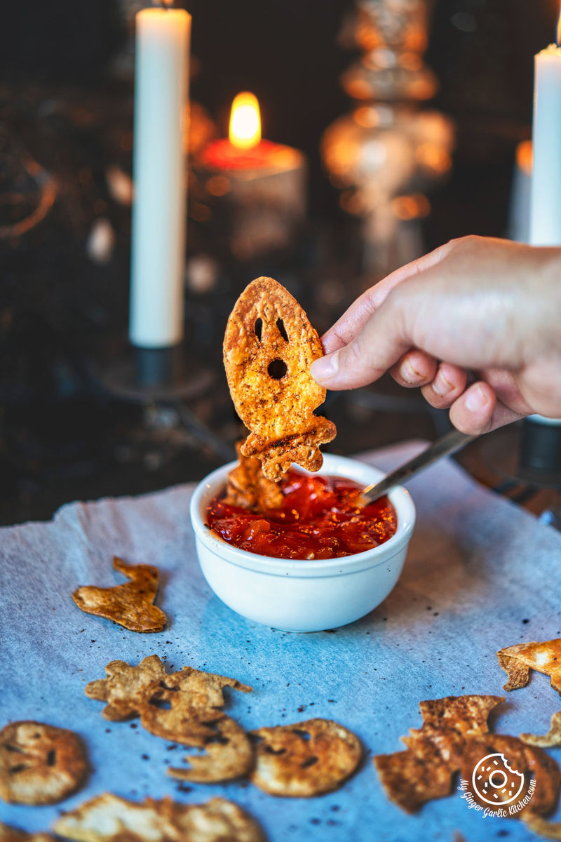 a white plate of halloween chips with a small bowl of red tomato salsa on top of it