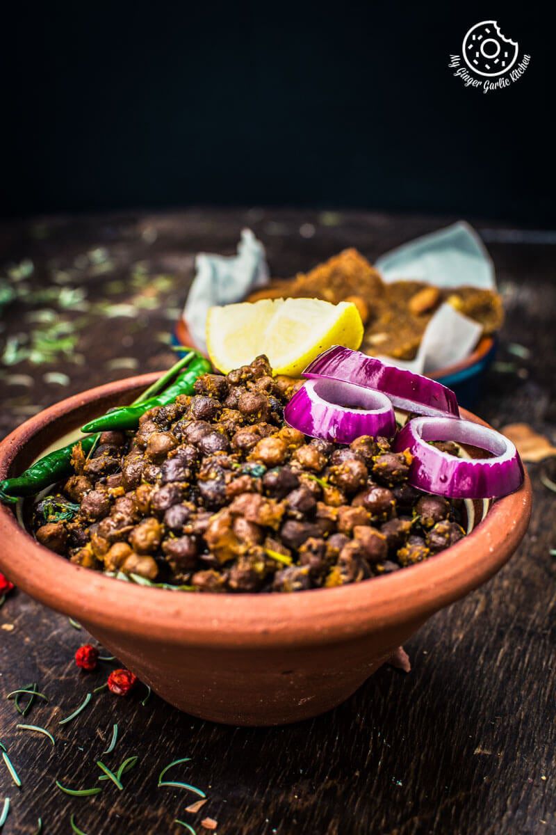 there is a bowl of kala chana with a green chilies, and lemon wedge on top