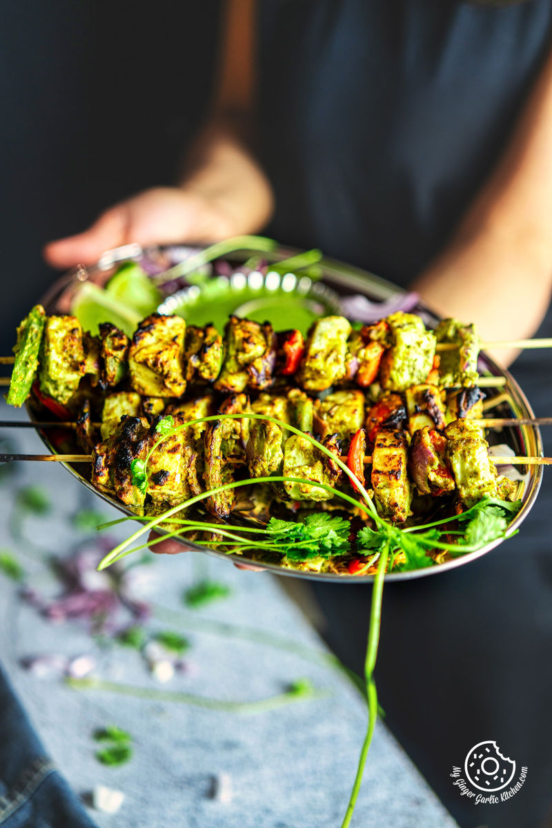 photo of a person holding a plate of Hariyali Paneer Tikka with skewers