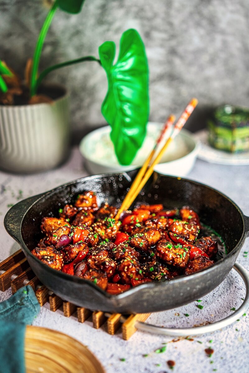 Crispy hoisin tofu stir fry served in a cast iron skillet with vegetables, garnished with chives and sesame seeds
