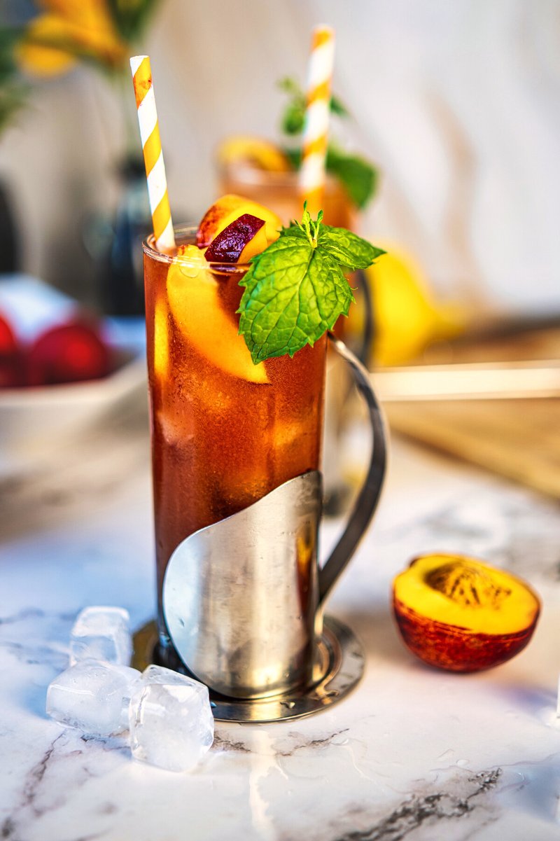 Homemade peach iced tea with fresh peach garnish, mint and ice cubes in a tall glass