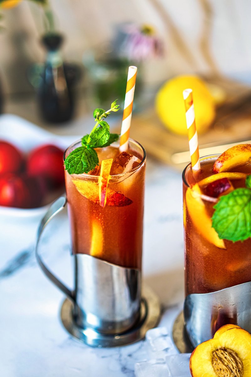 Peach iced tea with fresh peach slices, mint leaves and ice served in a tall glass