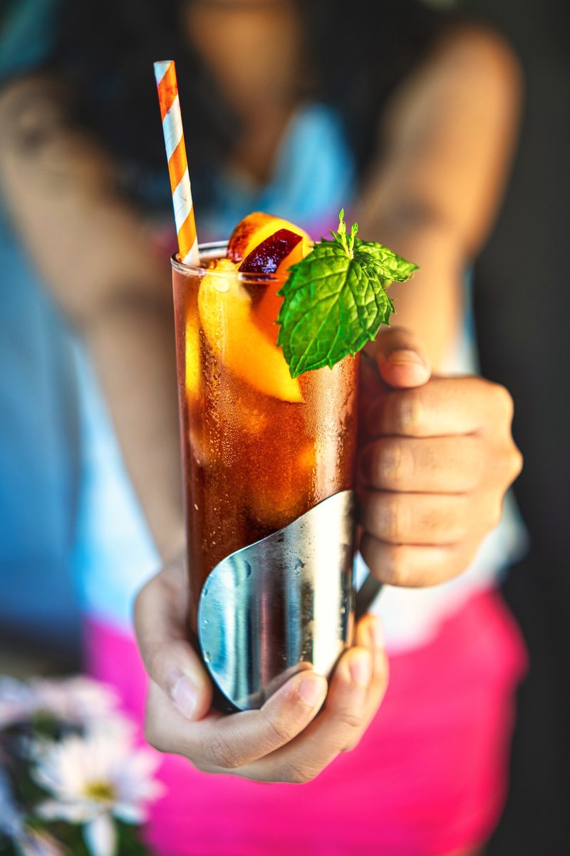 Fresh peach iced tea served in a glass with peach slices, mint and striped straw