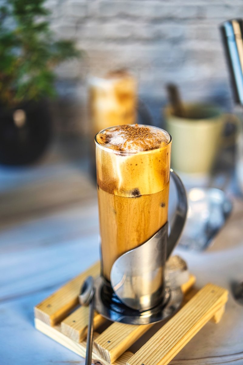 Honey Cinnamon Iced Coffee in a tall glass with whipped coffee foam, cinnamon, ice cubes, and a metal straw