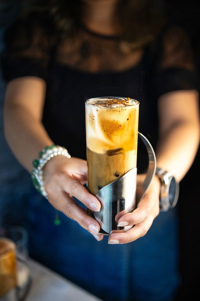 Homemade Honey Cinnamon Iced Coffee held in a glass with whipped coffee foam, cinnamon milk, ice, and cinnamon topping