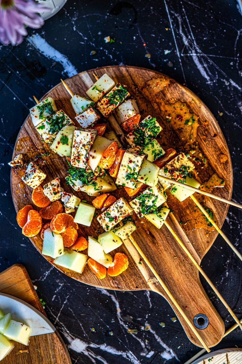 Overhead view of Honeydew Melon Feta Skewers with mandarins, herbed feta, and orange mustard vinaigrette on a wooden board