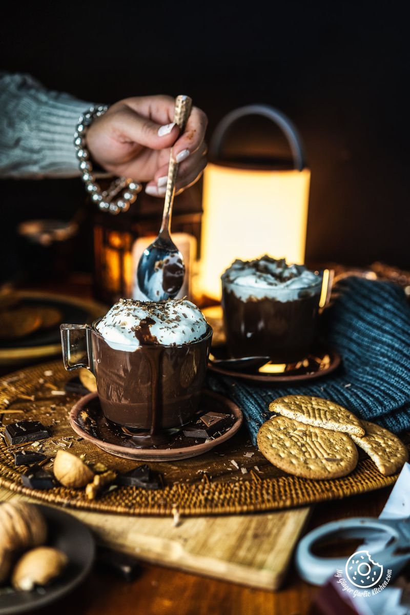 a women holing a spoon over Italian Hot Chocolate mug topped with whipped cream and chocolate shavings