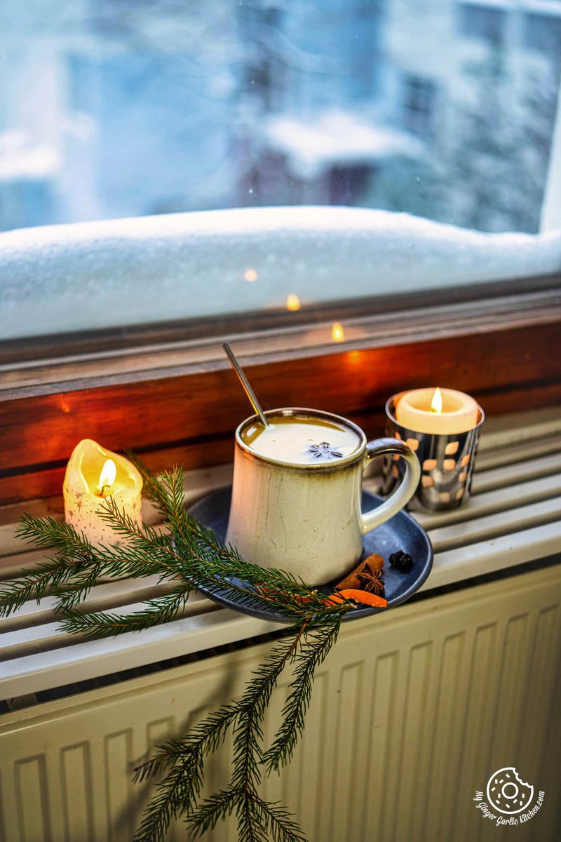 there is a cup of hot orange juice and two candles on a window sill