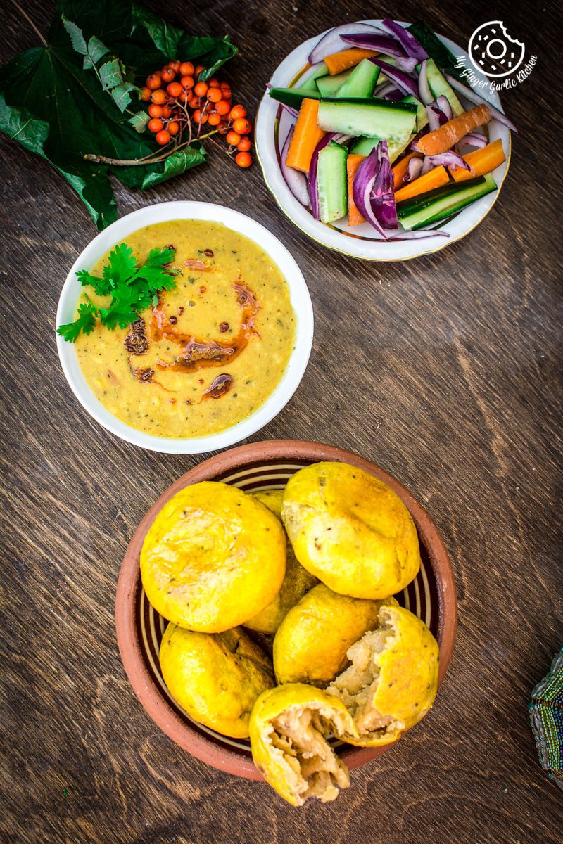 there is a bowl of bafla baati with a bowl of dal and sald on a table