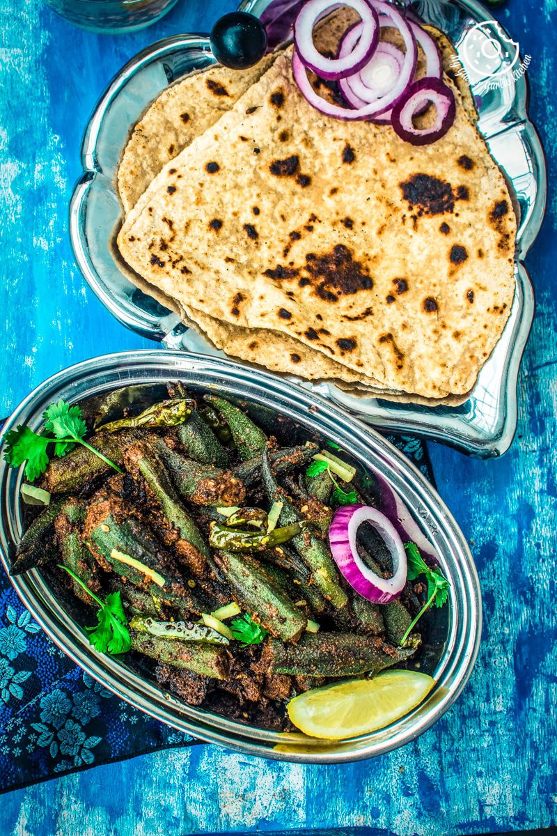 a plate of bharwa bhindi stuffed or okra masala on a blue table with some triangle paratha