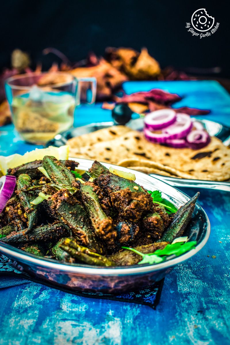 a plate of bharwa bhindi stuffed or okra masala on a blue table with some triangle parathas on a blue table