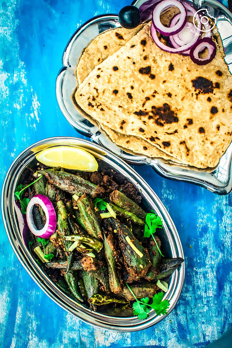 a plate of bharwa bhindi or stuffed okra masala on a blue table with some triangle parathas on a blue table