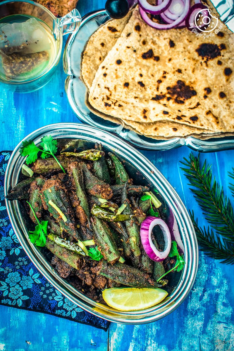 a plate of bharwa bhindi or stuffed okra masala on a blue table with some triangle parathas on a blue table
