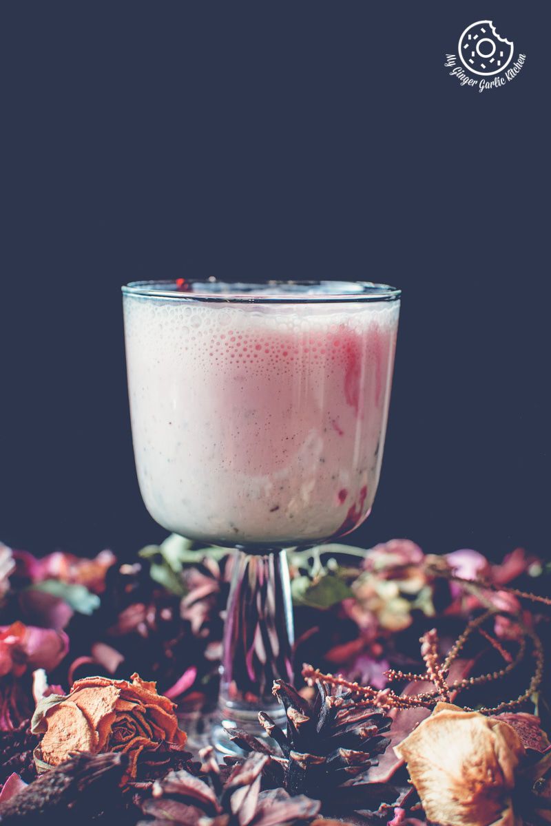 a glass of gulkand lassi aka rose lassi with dried flowers on a table