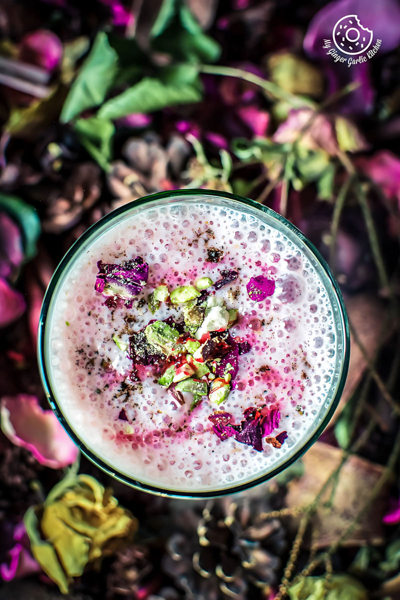 a glass of gulkand lassi or rose lassi with chopped pistachios and dried flowers on the top