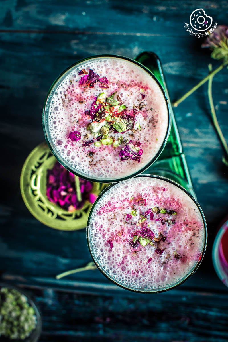 two glasses of gulkand lassi with flowers on a green plate