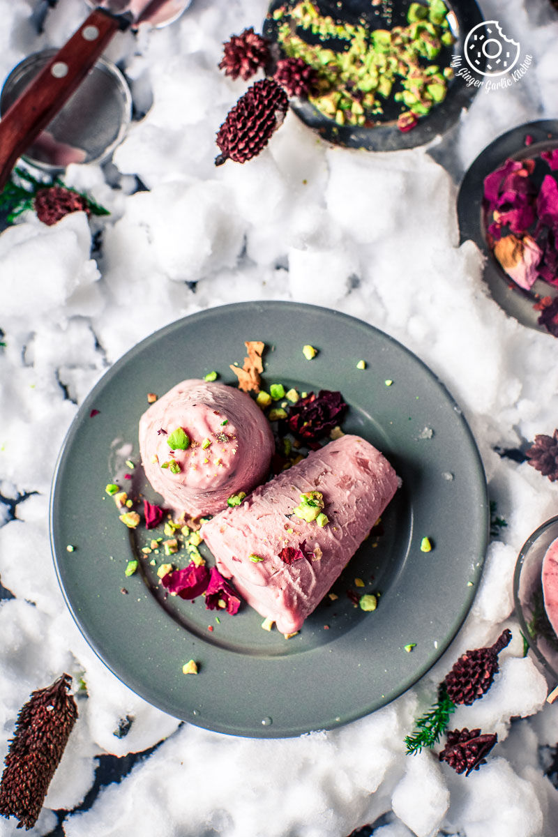 two rose kulfi topped with pistachios and dried rose petals on a plate on a table