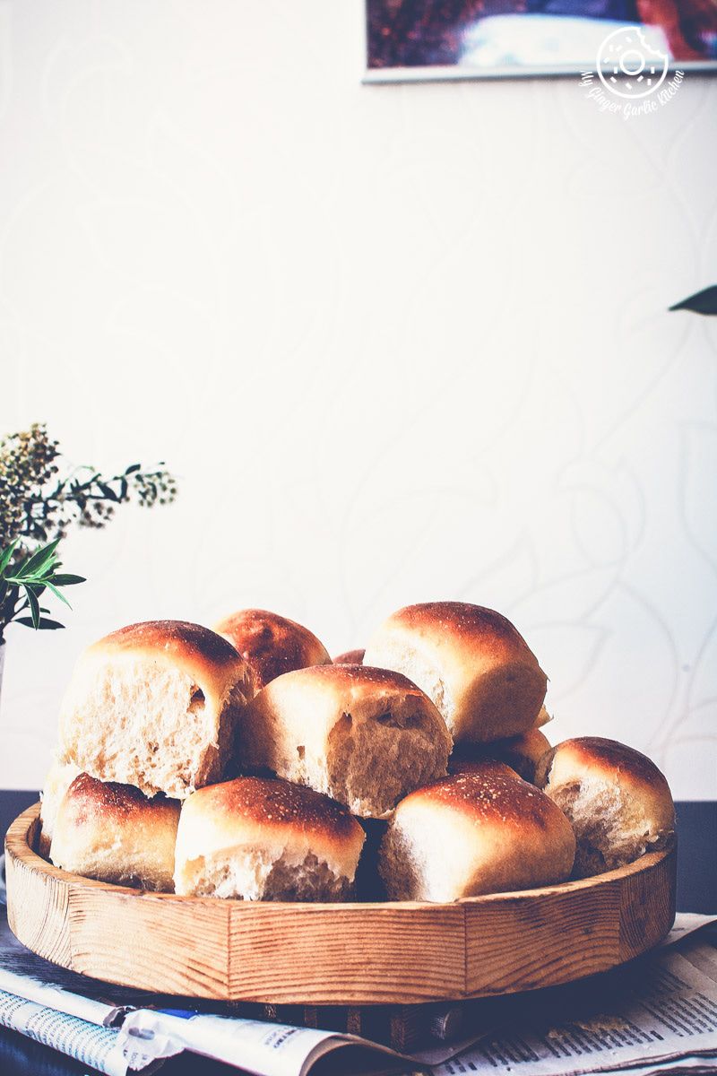 a bunch of ladi pav or dinner rolls on a wooden plate on a table