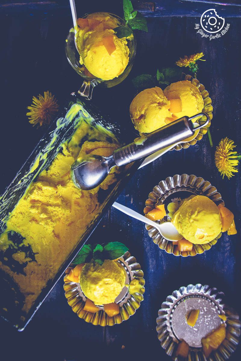 a tray of homemade mango ice cream with a spoon and scoops of mango ice cream